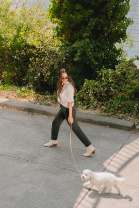 A woman walking on along the water on a path with her white dog on a leash