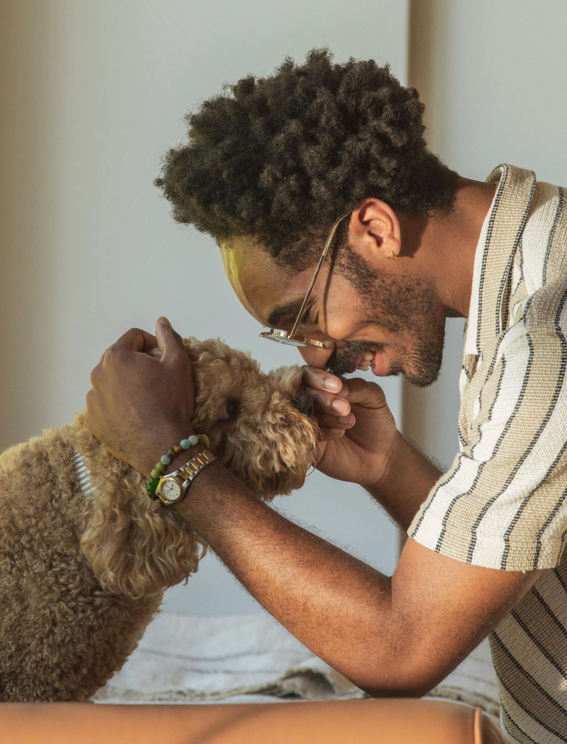 A man petting the head and touching noses of a golden doodle dog.